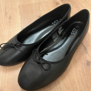 Svarta ballerinaskor med rosett - Klassiska svarta ballerinaskor med rund tå och söt liten rosett framtill. Skorna har en platt sula och är tillverkade i syntetmaterial med en matt finish. Perfekta för en stilren och enkel look. Köpta för 200kr och är oanvända, därför priset men går att diskutera vid snabb affär💗