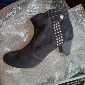 Svarta boots med nitar och klack - Snygga svarta boots i mocka-look med markerad klack och dekorativa silverfärgade nitar på sidan. Skorna har rund tå och synliga sömmar som ger en cool touch. Perfekta för dig som gillar en edgy stil.