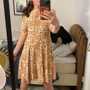Kort klänning med leopardmönster - Säljer en superfin kort klänning med leopardmönster i beige, brunt och orange. Klänningen har rund hals, halvlånga ärmar och ett flowy fall. Perfekt för dig som vill sticka ut med ett djurmönster! Materialet känns mjukt och följsamt.