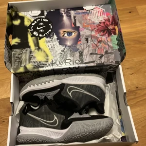 Nike Kyrie 4 low - Snygga Nike Kyrie sneakers i svart och grått med vit sula och tydlig Swoosh-logga på sidan. Skorna har coolt mönstrad yttersula med Kyrie Irving-logga undertill och snörning för perfekt passform. Ovandelen är i syntetmaterial med rutstruktur för extra stilpoäng.