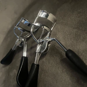 Två ögonfransböjare i metall - Säljer två klassiska ögonfransböjare i silverfärgad metall med svarta, ergonomiska handtag i plast. Perfekta för att få till snyggt böjda fransar snabbt. Smidig design som passar de flesta ögonformer.