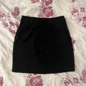 Svart kortkjol från ONLY - Svart kortkjol från ONLY i mjukt material i storlek XS. Kjolen har resår i midjan, knytband framtill och bälteshällor. Passar till allt och är superenkel att styla. 