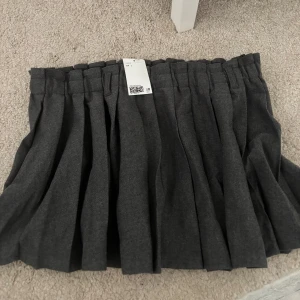 Grå plisserad kjol - Snygg grå plisserad kjol med en klassisk design. Perfekt för en stilren look. Kjolen har en elastisk midja för extra komfort och passar till många olika tillfällen.
