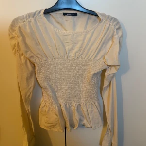 Beige långärmad blus från Gina Tricot - Beige blus från Gina Tricot med smockdetaljer i midjan och långa ärmar. Strl S
