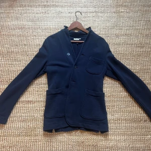 Mörkblå kavaj med knappar - Snygg mörkblå kavaj med knappar framtill och tre fickor. Perfekt för en stilren look. Passar bra till både vardag och mer uppklädda tillfällen.