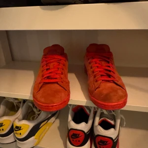 Röda sneakers från Adidas - Snygga röda sneakers från Adidas med en stilren design. Skorna har en rund tå och är tillverkade i mocka med matchande röda snören. Perfekta för en casual look.