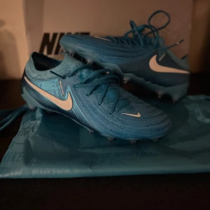 Nike phantom gx elite - Snygga blå Nike fotbollsskor med vit swoosh och snörning. Perfekta för fotbollsplanen med en modern design och bra grepp. Startpris 1800 och högstbudande. Det är bara att höra av dig vid frågor/funderingar