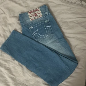 Ljusblå jeans från True Religion - Snygga ljusblå jeans från True Religion med klassisk femficksdesign och kontrasterande sömmar. Jeansen har en broderad logga på bakfickorna och en patch med varumärket på baksidan av midjan. Perfekta för en avslappnad stil. Köpta här på plick men passade tyvärr inte mig
