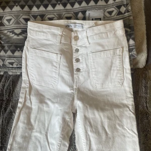 Vita byxor från Zara - Snygga vita byxor från Zara med hög midja och raka ben. Byxorna har framträdande knappar och stora fickor framtill. Perfekta för en stilren look.