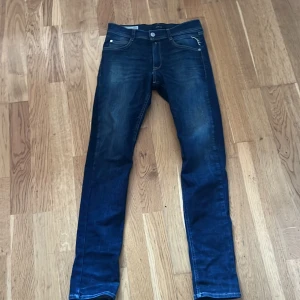 Mörkblå jeans från Replay - Snygga mörkblå jeans från Replay med en klassisk femficksdesign och diskreta slitningar. De har en normal passform och är perfekta för en avslappnad stil. Märkeslogga på baksidan och knappgylf framtill, pris är ej hugget i sten.