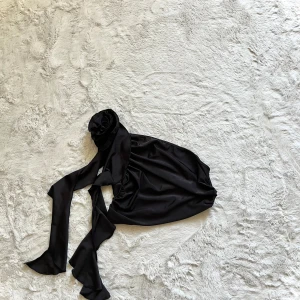 Svart axelbandslös topp - Snygg svart axelbandslös topp med knytband. Perfekt för en stilren look. Materialet är mjukt och följsamt, vilket ger en bekväm passform. Passar utmärkt till både jeans och kjol.