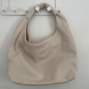 Beige axelväska från Gina - Snygg beige axelväska från Gina med en enkel och stilren design. Väskan har en praktisk dragkedja på insidan för säker förvaring. Den är större än vad det framstår som så man får plats med mycket.
