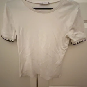 Vit kortärmad topp från Zara - Säljer en enkel t-shirt med fina detaljer, tröjan är knappt använd och är i bra skick. Den är i storlek M men är mer som en S 