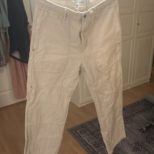 Beige byxor från Bershka - Säljer ett par beige byxor från Bershka. Byxorna har en avslappnad passform med elastisk midja och knappstängning. Perfekta för en casual look.