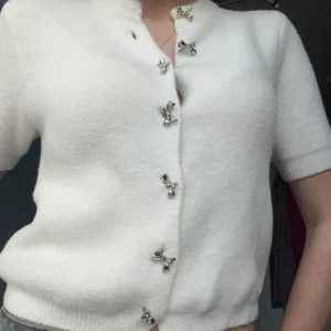 Zara Stickad tröja med rosetter - Säljer en stilren vit kofta med korta ärmar och unika dekorativa knappar i form av små rosetter Koftan är mjuk och bekväm. Ny med lappen kvar🌷 Perfekt till våren. 