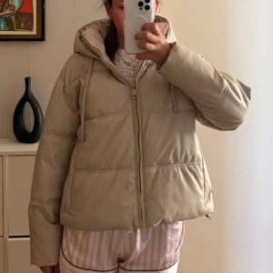 Beige pufferjacka från Zara - Säljer en snygg beige pufferjacka från Zara med huva och dragkedja. Jackan har en modern look och är perfekt för kyligare dagar. Den är både stilren och praktisk med sin vadderade design. Knappt använd