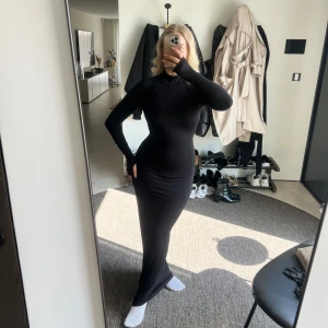 Svart långklänning med öppen rygg - Svart tight klänning med öppen rygg, polokrage och öppning för tummarna vid ärmarna. Endast använd en gång. I storlek S från Ginatricot.