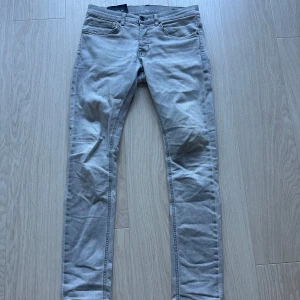 Grå jeans från Dondup - Snygga grå jeans från Dondup med en klassisk femficksdesign. De har en knappgylf och är tillverkade i ett bekvämt material som ger en stilren look. Perfekta för en avslappnad stil. Dom är i storlek 32 men sitter som 31 och är varsamt använda.