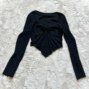 Svart långärmad topp - Snygg svart långärmad topp med en unik twistdetalj framtill. Toppen har en croppad design och är perfekt för en trendig look.