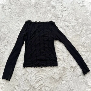 Svart långärmad topp i mesh - Snygg svart långärmad topp med transparenta detaljer och vågiga kanter. Perfekt för en stilren look. Toppen har en unik design med vågiga sömmar som ger en extra touch.