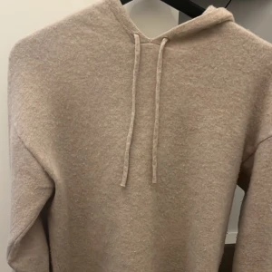 Beige kashmir hoodie från Carmés - Säljer en mysig beige hoodie från Carmés i storlek S. Tröjan har en mjuk och fluffig yta med dragsko i huvan. Perfekt för kyliga dagar!