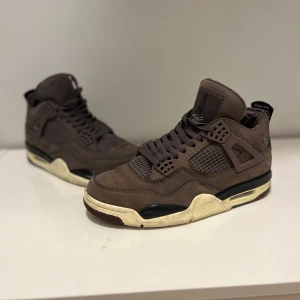 Jordan 4 - Snygga bruna Nike Air sneakers i mocka med klassisk design. Skorna har en rund tå och snörning framtill. Perfekta för dig som vill ha en stilren look med en touch av retro.