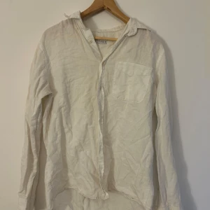 Vit linneskjorta från H&M - Säljer en stilren vit linneskjorta från H&M. Skjortan har en klassisk krage och en bröstficka. Perfekt för en avslappnad look med sin luftiga passform och långa ärmar. Passar bra till både jeans och chinos.