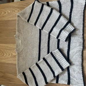 Beige och svart randig stickad tröja från Pull&Bear - Säljer en snygg beige stickad tröja från Pull&Bear med svarta ränder. Tröjan har en klassisk rund hals och långa ärmar. Perfekt för kyligare dagar!