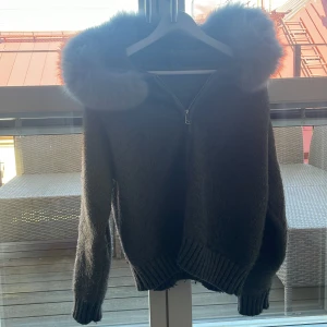 Grå stickad jacka med pälshuva - Säljer en mysig grå stickad jacka från alessa med en fluffig pälshuva. Jackan har dragkedja framtill och långa ärmar med ribbade muddar. Har inte haft den speciellt länge. Bra jacka till våren.