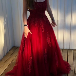 Röd balklänning med spetsdetaljer - Elegant röd balklänning med vackra spetsdetaljer och snörning i ryggen. Klänningen har en lång och fluffig kjol med flera olika lager. Klänningen är ganska lång! Jag är 160 cm lång och klänningen släppas. Kontakta innan köp❤️