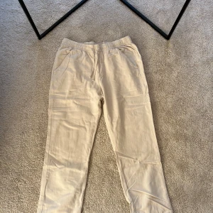 Beige linnebyxor med resårmidja - Säljer ett par bekväma beige linnebyxor med resårmidja och snörning. Byxorna har en avslappnad passform och är perfekta för varma dagar. De har praktiska fickor på sidorna.