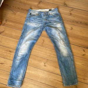 Jack&jones Erik Anti Fit - Säljer ett par blå jeansbyxor från Erik med en anti fit design. W32 L34. Byxorna har en klassisk femficksmodell och en ljus tvätt med slitningar för en avslappnad look. Perfekta nu till våren.