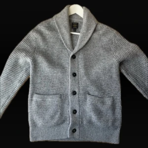 Grå stickad kofta med knappar - Säljer en stilren grå stickad kofta med knappar och två praktiska fickor framtill. Koftan har en elegant krage och är perfekt för kyligare dagar. Passar både till vardags och mer uppklädda tillfällen. S men är med som M