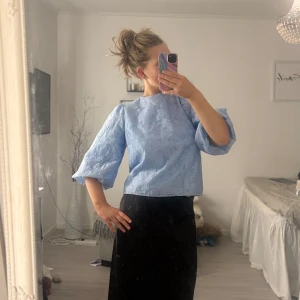 Blå blus med rosett - Söt ljusblå blus med puffiga trekvartsärmar och vackert blommigt mönster. Blusen har en öppen rygg med två stora rosetter som ger en extra touch. Perfekt för en stilren och feminin look. Slutsåld på hemsidan 