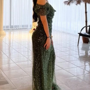 Grön glittrig långklänning - Säljer en fantastisk grön glittrig långklänning med offshoulder-design. Klänningen har en elegant passform och är perfekt för speciella tillfällen. Den glittriga ytan ger en extra touch av glamour.använd bara en gång storlek S/M