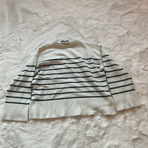 Vit och svart randig tröja från 157 - Säljer en snygg vit tröja med svarta ränder från 157. Tröjan har en normal passform och är långärmad med ribbade muddar vid ärmslut och nederkant. Perfekt för en stilren look!