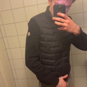 Moncler navy blå cardigan - Snygg svart och blå cardigan med dragkedja. Jackan har långa ärmar och en quiltad design framtill. Perfekt för kyligare dagar. L passar som M