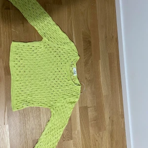 Gul stickad tröja från H&M - Säljer en ljus neongrön stickad tröja från H&M med ett snyggt hålmönster. Tröjan har långa ärmar och en bekväm passform. Den är nästan helt oanvänd och i väldigt bra skick! Hade passat en solig dag på stranden eller kanske en fest med temat 90-tal! Går att styla på många sätt!!💛😊🌼