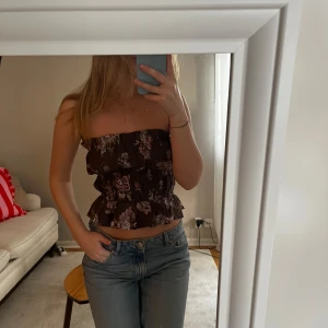 Blommig brun tubtopp från H&M x Brock Collection - Säljer en söt brun tubtopp från H&M x Brock Collection med blommigt mönster. Toppen har volangdetaljer och en smickrande passform. Passar toppen för XS men även mig som vanligtvis är en storlek S. Perfekt för en somrig look! 🌸
