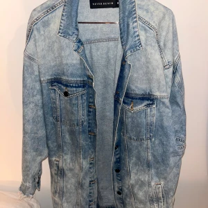 Ljusblå jeansjacka - Snygg ljusblå jeansjacka från Never Denim med klassisk krage och knappar framtill. Jackan har två bröstfickor med lock och knapp samt två sidofickor. På mig som är 168 går jackan ovanför knävecken 💙