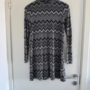 Svartvit klänning från Gina Tricot - Snygg svartvit klänning från Gina Tricot med ett zigzag-mönster. Klänningen har långa ärmar och en hög krage, perfekt för en stilren look. (Katt och kanin finns i hemmet) 