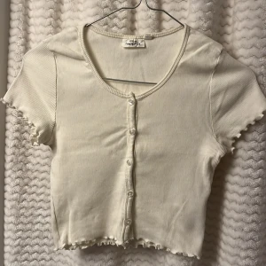Vit ribbad kortärmad topp från KappAhl🤍 - Säljer en söt vit ribbad topp från KappAhl med korta ärmar och knappar framtill. 🥥
