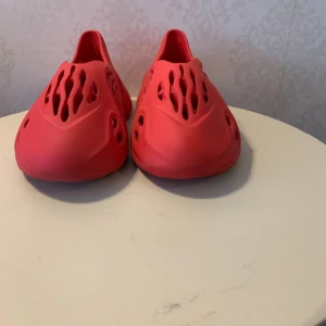 Röda Yeezy Foam Runners - Snygga röda Yeezy Foam Runners med ett unikt hålmönster som ger en modern och luftig känsla. Perfekta för en avslappnad stil och bekväma att bära hela dagen. Den djärva färgen gör dem till ett blickfång i varje outfit. Pris kan diskuteras!!