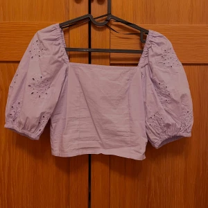 Ljuslila blus med puffärmar - Säljer en söt ljuslila blus med puffiga trekvartsärmar och broderade detaljer. Blusen har en fyrkantig halsringning och elastiska ärmslut. Perfekt för en somrig look!