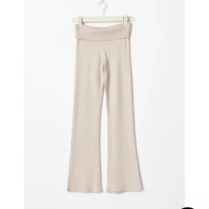 Beige stickade byxor - Snygga beige stickade byxor med låg midja och ribbad detalj i midjan. Byxorna har en bootcut-stil som ger en trendig look. Perfekta för en avslappnad och stilren outfit.