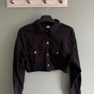 Svart croppad jeansjacka  - Croppad/kort svart jeansjacka med fickor.  I storlek S.