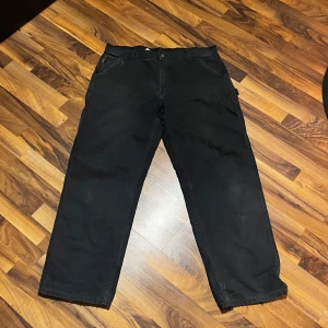 Svarta carhartt byxor - Säljer ett par svarta byxor med raka ben och normal passform. Byxorna har en klassisk design med knappar och dragkedja framtill. Perfekta för en stilren look. 34w, 38 L 