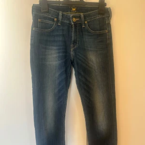 Mörkblå jeans från Lee (scarlett) W28 L31 - Snygga mörkblå jeans från Lee med klassisk femficksdesign och knappgylf. Jeansen har en rak /skinny passform och är perfekta för en avslappnad stil. De är tillverkade i ett slitstarkt denimtyg som ger en tidlös look.