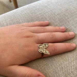 Silverfärgad ring med fjärilsdesign - Snygg guldfärgad ring med en glittrig fjärilsdesign. Perfekt för att lägga till en touch av elegans till din stil. Ringen har en justerbar passform för att passa olika storlekar. En detalj är bara att den har jätte lite rost på kanten