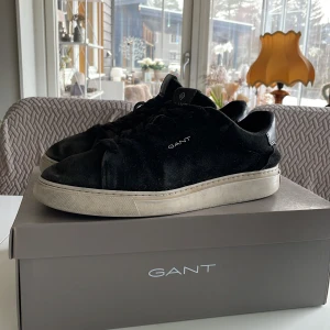 Svarta sneakers från Gant - Snygga svarta sneakers från Gant i mocka med vit sula och röd undersida. Skorna har snörning och en stilren design som passar perfekt till vardags. Storlek 43